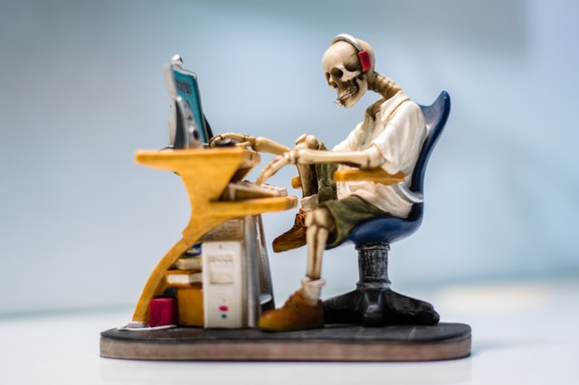 painted sculpture of human skeleton sitting at a computer